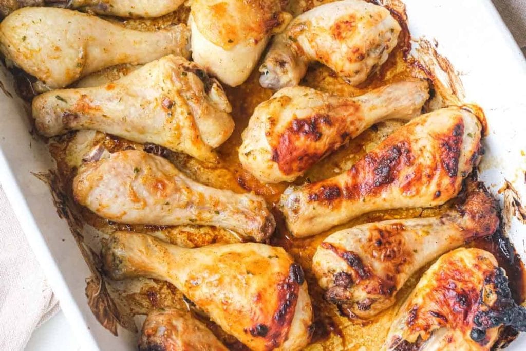 Baked chicken drumsticks in a white dish, some browned and crispy, others light and tender, with visible juices and seasonings.