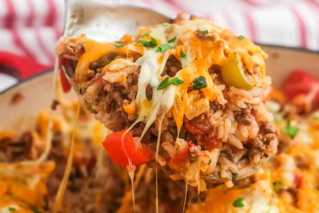 Close-up of a spoonful of cheesy stuffed pepper casserole with ground beef, rice, green pepper, tomatoes, and melted cheese, garnished with parsley.