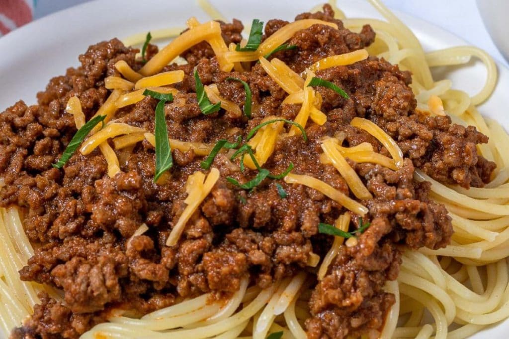 A plate of spaghetti topped with ground beef, shredded cheese, and garnished with fresh herbs.