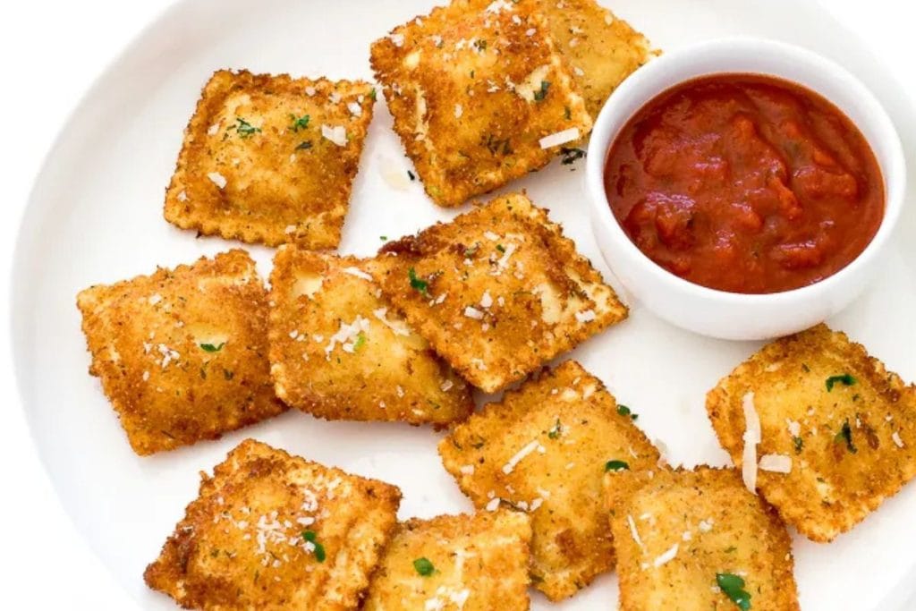 Plate of fried ravioli garnished with herbs and grated cheese, served with a side of marinara sauce in a small bowl.
