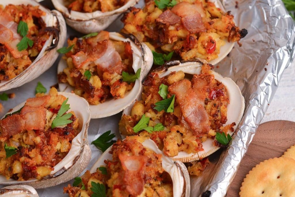 Baked stuffed clams topped with crispy bacon and parsley on a foil-lined tray.