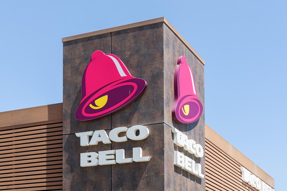 Taco Bell restaurant exterior with logo, featuring a pink bell, against a clear blue sky.