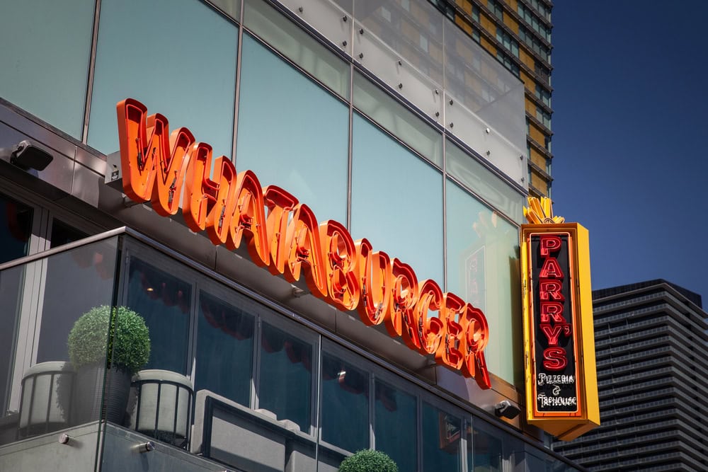 Exterior of a building featuring bright orange "WHATABURGER" sign and a neon "PARRY'S Pizzeria & Taphouse" sign against a blue sky.