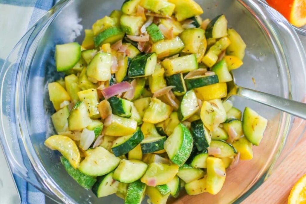 Bowl of mixed sautéed zucchini and yellow squash with red onion pieces, served in a glass bowl with a spoon.