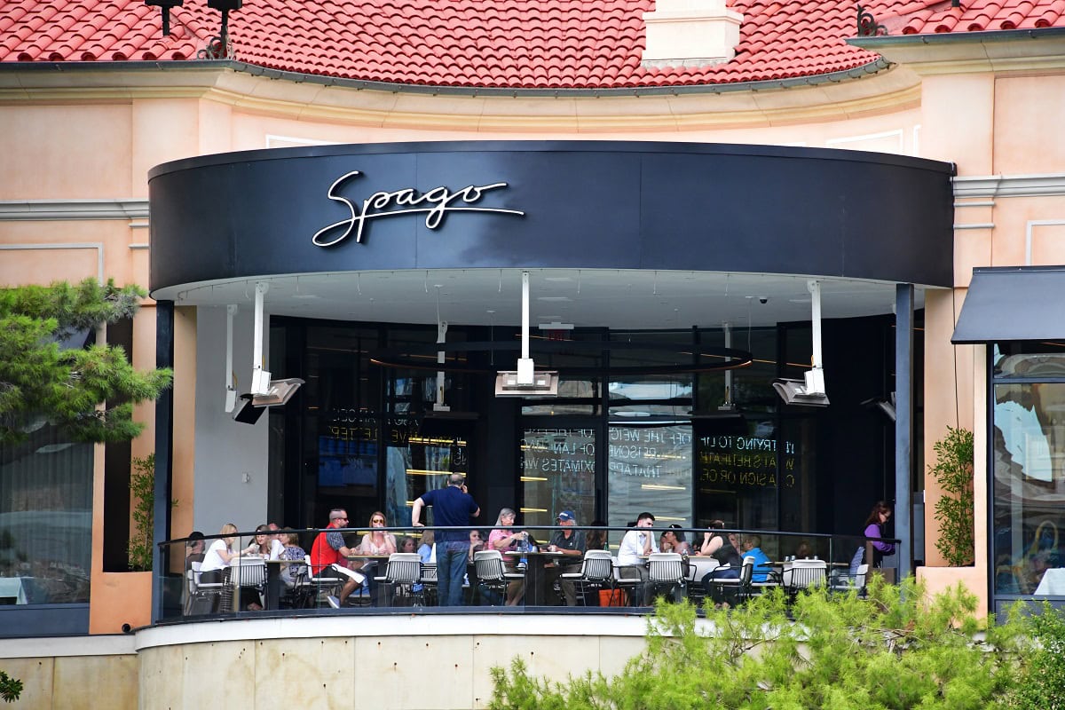 People dining at an outdoor terrace of a restaurant named Spago under a curved roof with red tiles.