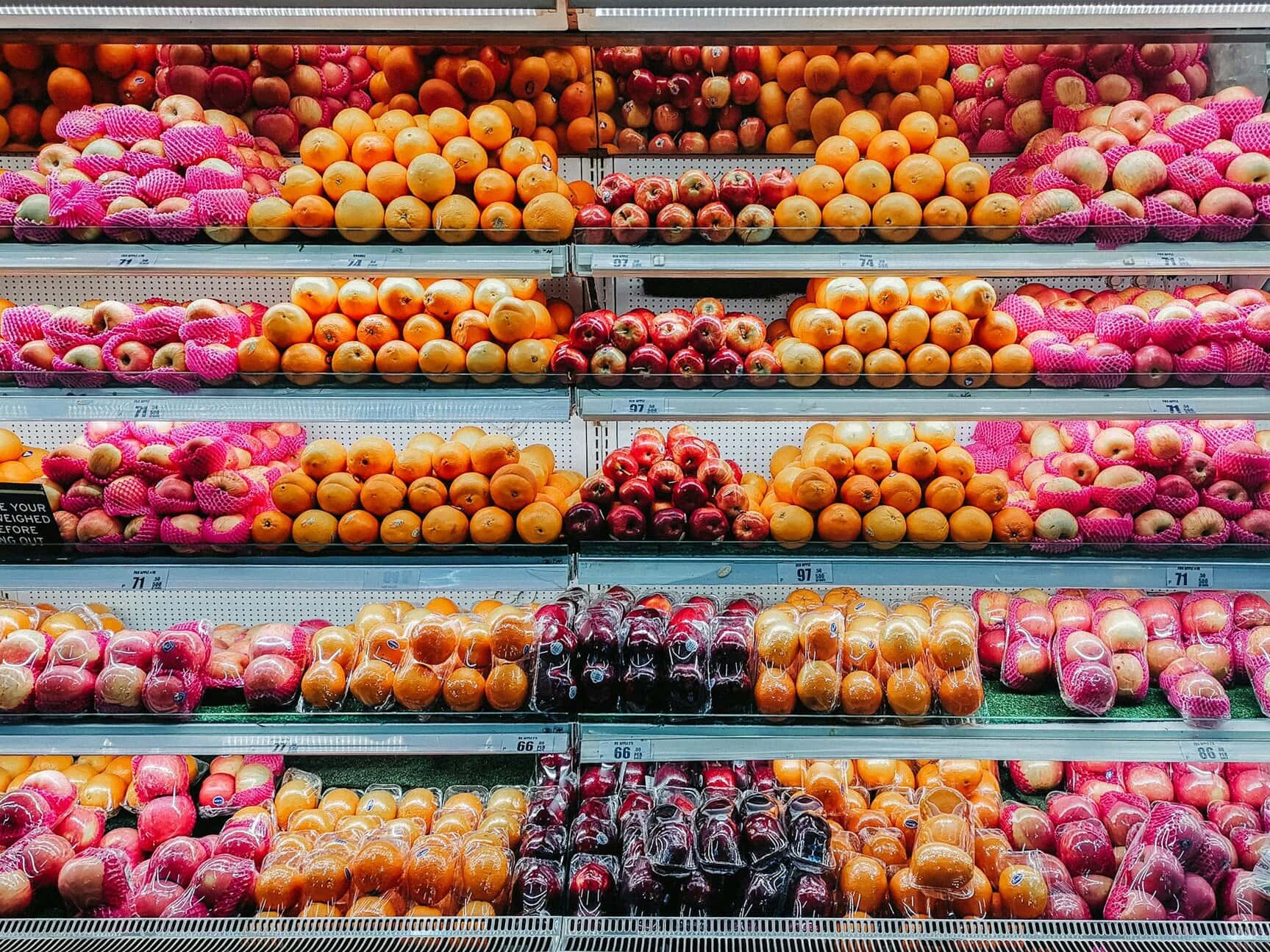 Supermarket shelf with various fruits, including apples, oranges, and grapefruits, neatly arranged in netted packaging.