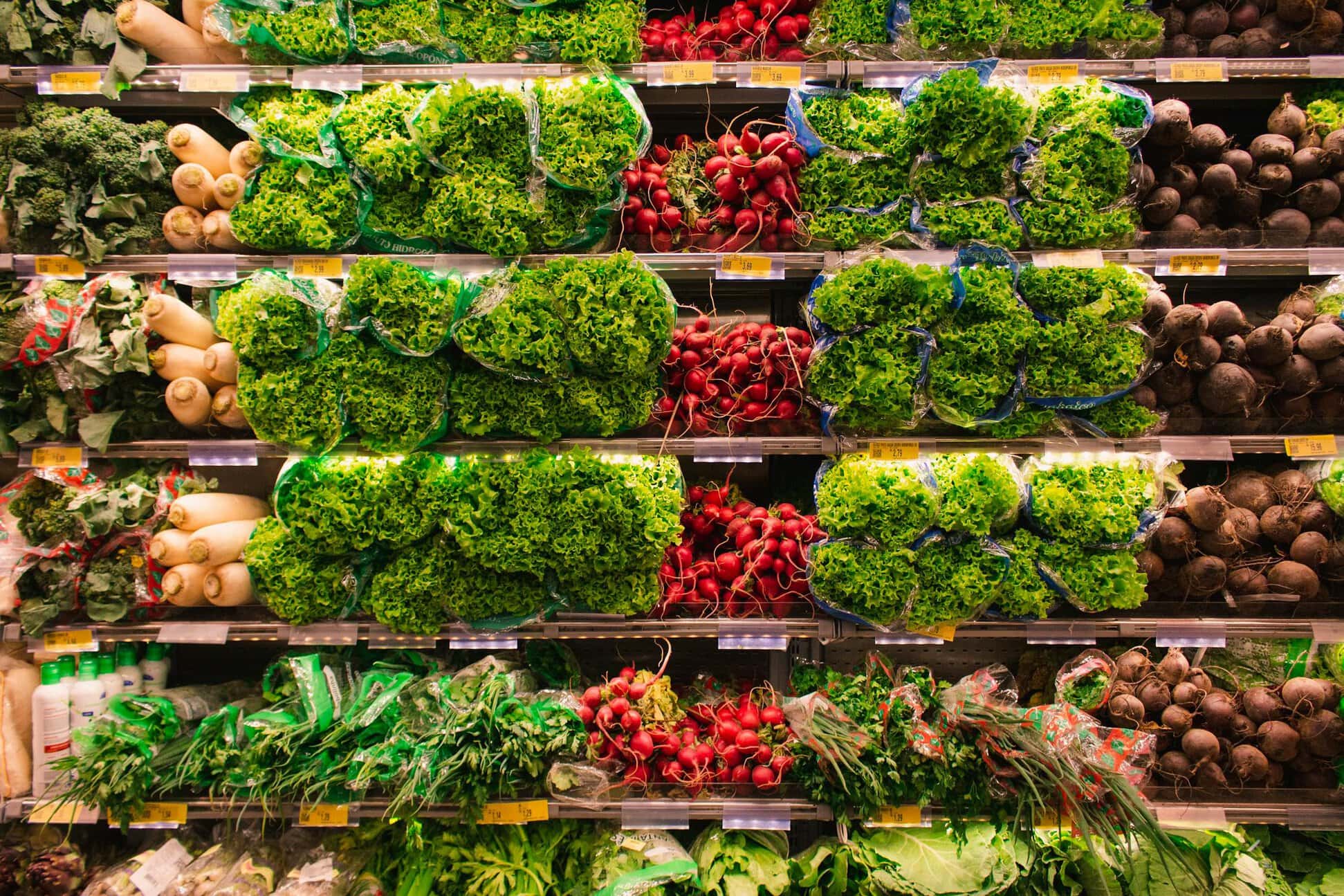 A grocery store produce section displaying various vegetables, including lettuce, radishes, beets, and leafy greens, neatly organized on shelves.