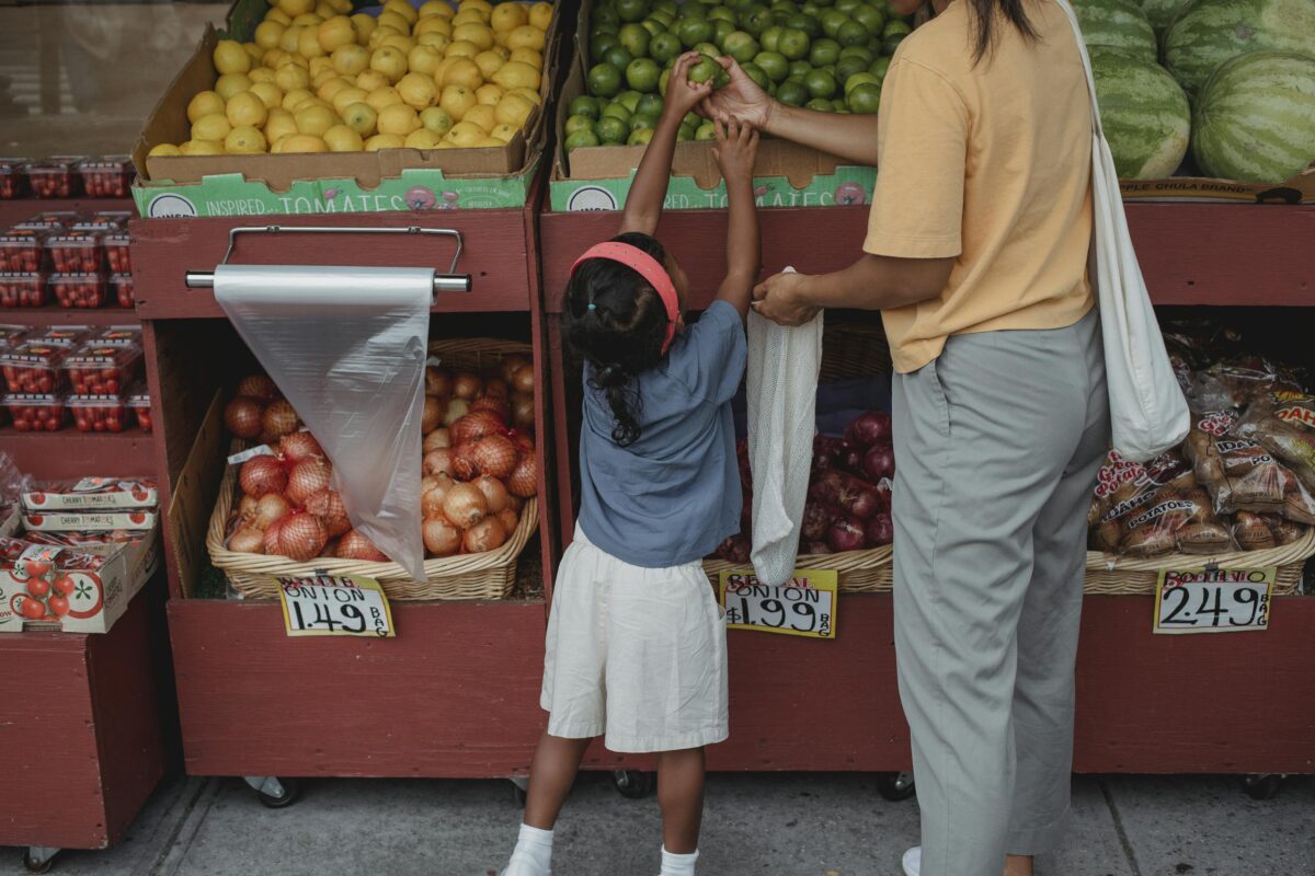 A mother and daughter selecting fruits and vegetables at an outdoor market.