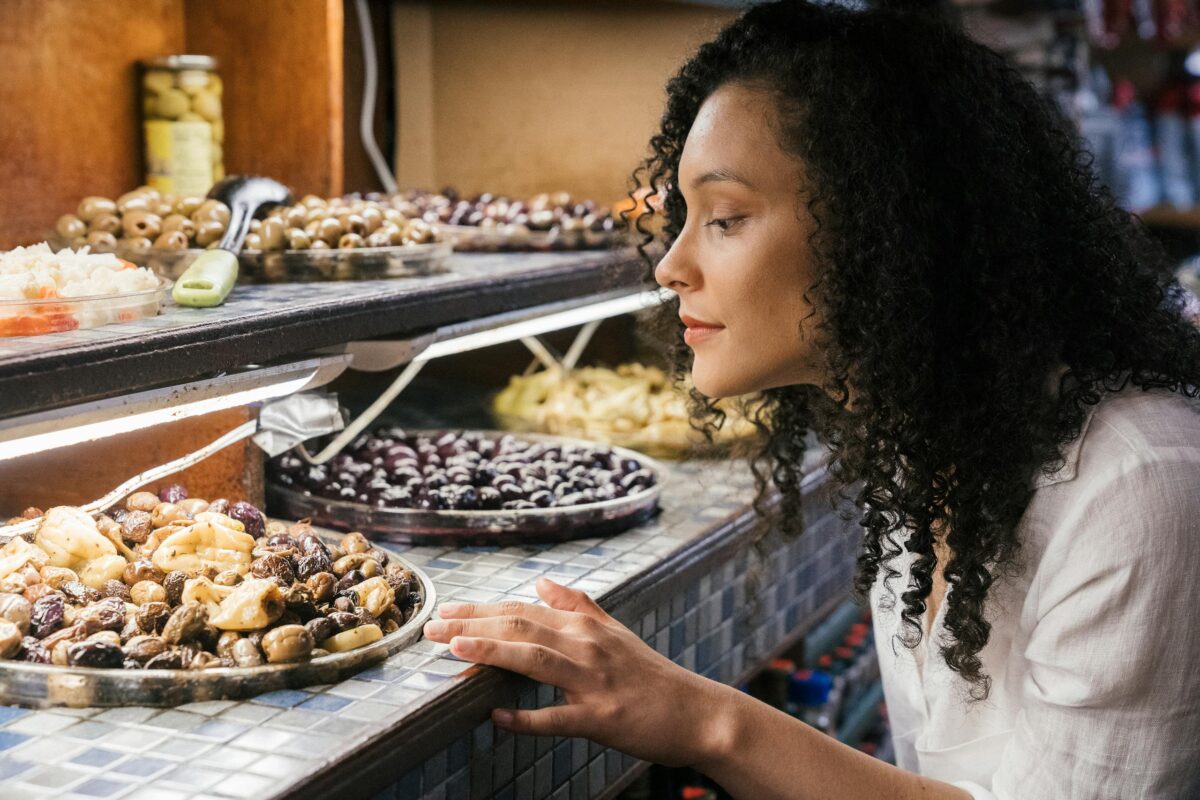 A woman observes a display filled with a variety of olives and other foods.