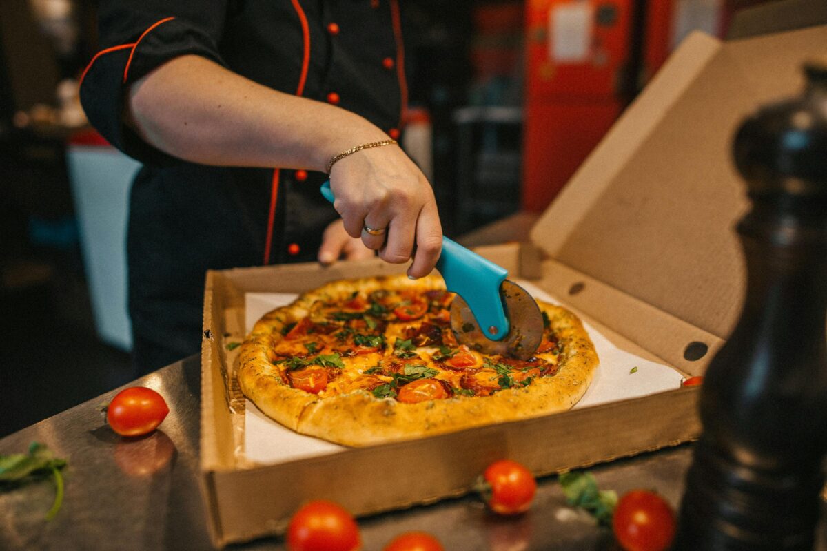 Close-up of a chef slicing a freshly baked pizza with a cutter in a kitchen. Vibrant ingredients on a rustic crust.